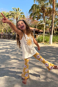Girl wearing the Yellow Sun Cotton Set with a sequined sun vest and flared trousers while laughing on a beach.