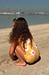 Girl wearing the yellow sun print swimsuit with frill detailing while crouching on a sandy beach.