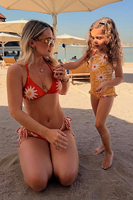 Girl's yellow sun-printed swimsuit with frill detailing on a beach vacation with a matching adult bikini.