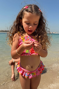 Young girl wearing the Girls Pink Fruit Crop Bikini Set with a shirred bandeau top and ruffle bottoms at the beach.