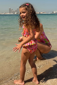 Girls Pink Fruit Crop Bikini Set with Mediterranean fruit print and frill details on a sunny beach.