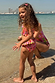 Girls Pink Fruit Crop Bikini Set with Mediterranean fruit print and frill details on a sunny beach.