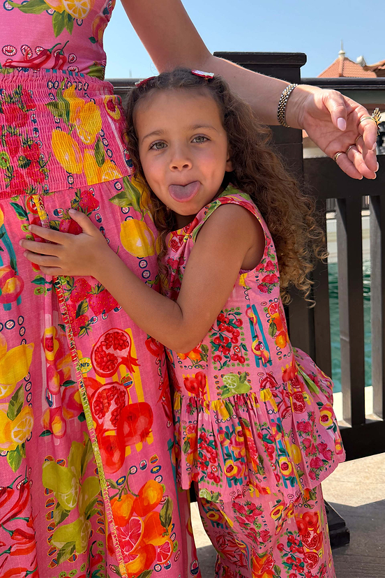 Girl's pink fruit print peplum top and wide leg set, hugging an adult in a matching print while on vacation.