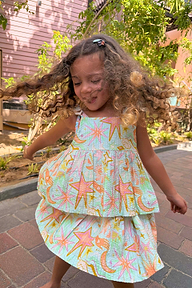 Young girl spinning in the blue Starburst Skirt Co-ord Set with peplum top and tiered sun and star print skirt.