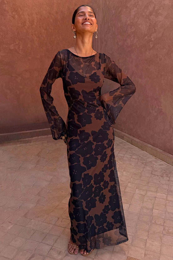 Model wearing the Mesh Dress in Tan Jaden Floral Print against a textured terracotta background.