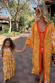 Girl's yellow cotton maxi sun dress with a white sun print and shirred top, walking outdoors on vacation.