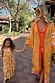 Girl's yellow cotton maxi sun dress with a white sun print and shirred top, walking outdoors on vacation.