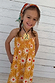 Girl wearing a yellow cotton maxi sun dress with a sun print and shirred bodice against a wooden wall.
