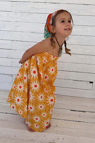 Yellow cotton maxi sun dress with a shirred top and sun print pattern worn by a young girl.