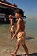 Boy's Yellow Sun Swim Shorts with a soleil print, worn by two boys walking in shallow beach water.