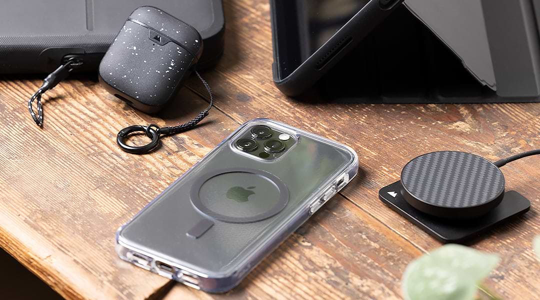 Desk with black MacBook sleeve, black iPad case, wireless charger and a clear phone case