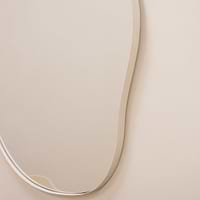 Ecru metal pond shaped irregular wall mirror displayed on wall closeup