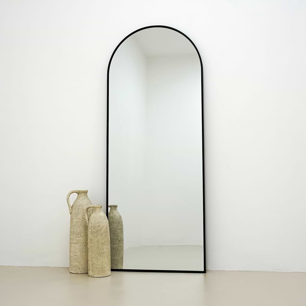 Black Full Length Arched Metal Mirror beside ceramic vases