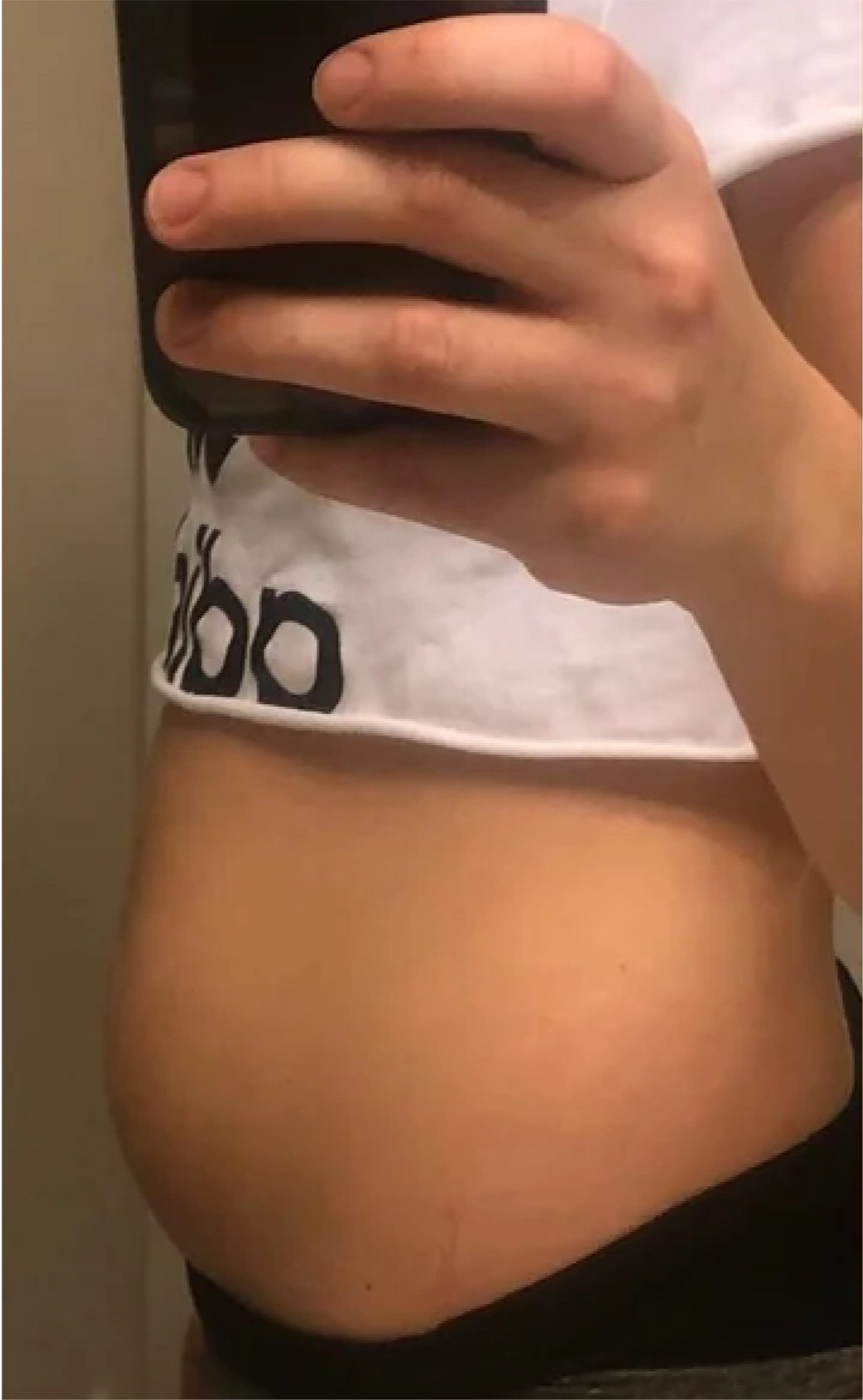 A person taking a mirror selfie, showing their side profile with a visible belly.