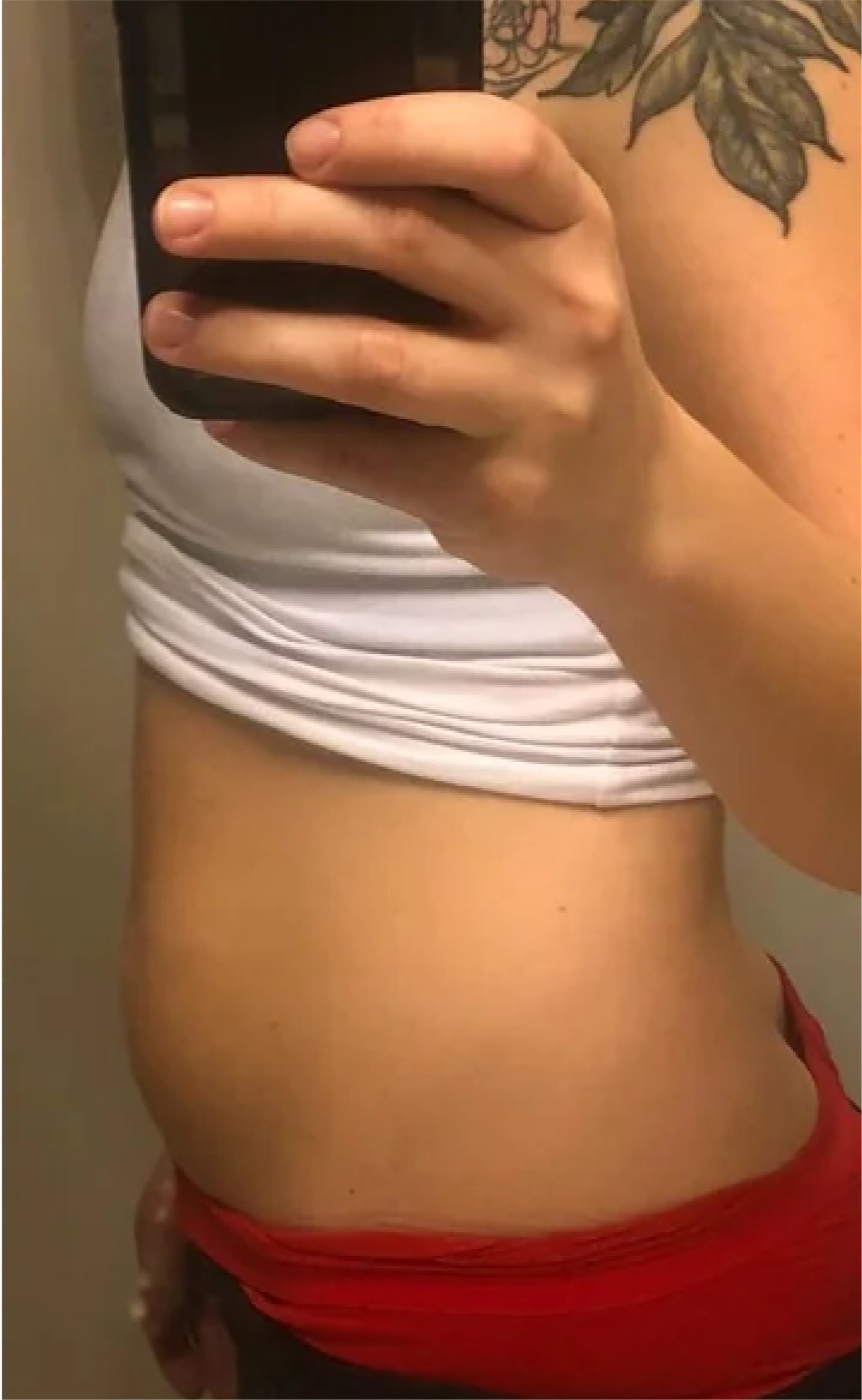 Person taking a mirror selfie showing a tattooed arm and midsection.