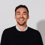 Smiling man in a black sweater against a plain background.