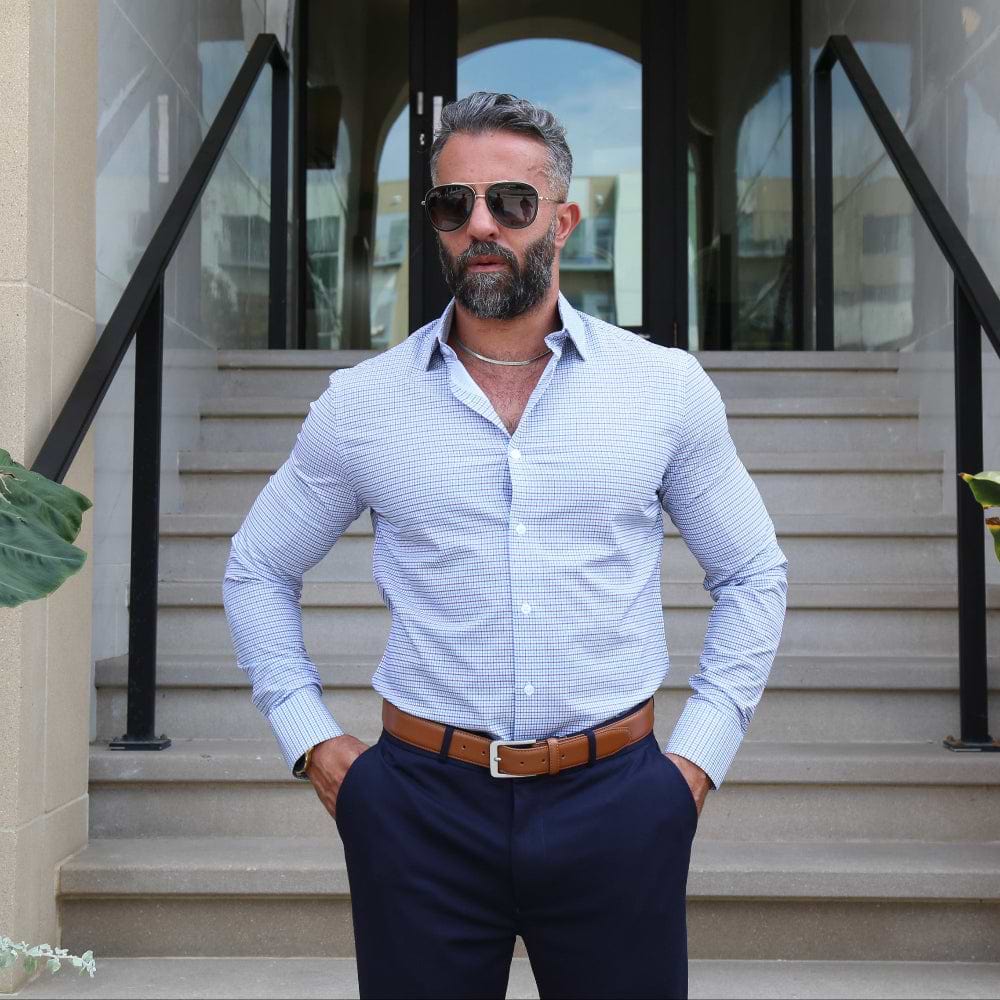 Man in a light blue shirt and dark pants standing on steps outside a building with plants around.