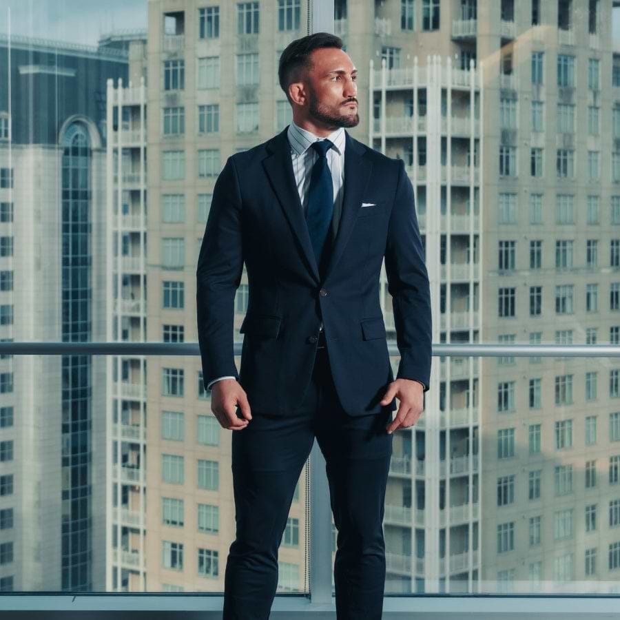 Man in a suit standing in front of a cityscape with tall buildings.