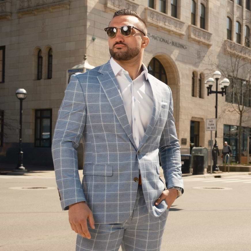 Man in a gray checkered suit standing on a city street corner.
