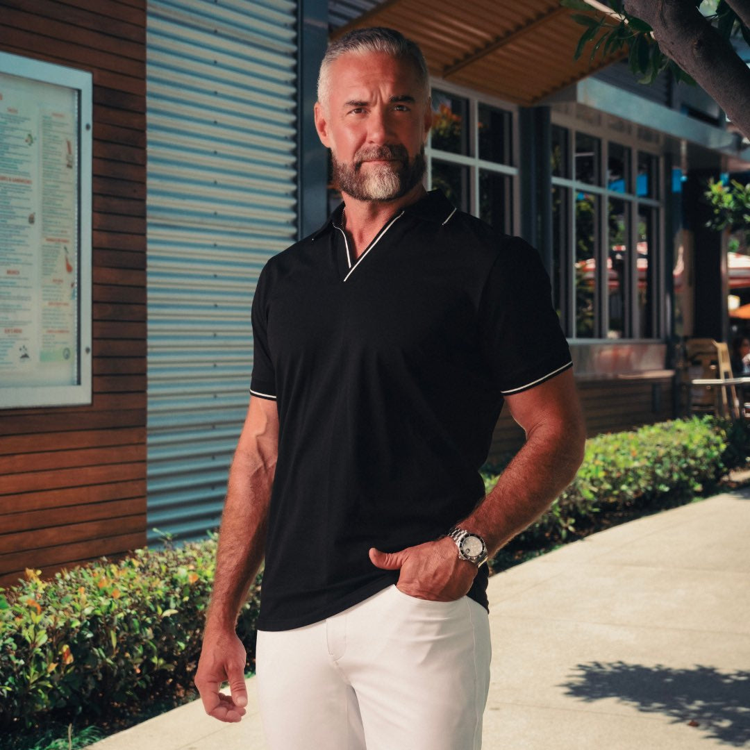 Man wearing a black polo shirt and white pants standing outdoors.