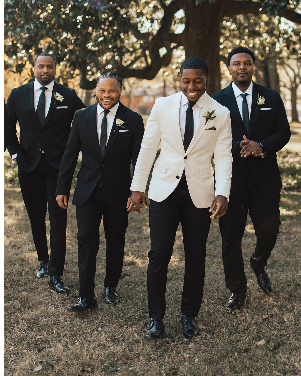 Four men in formal attire standing outdoors with trees in the background