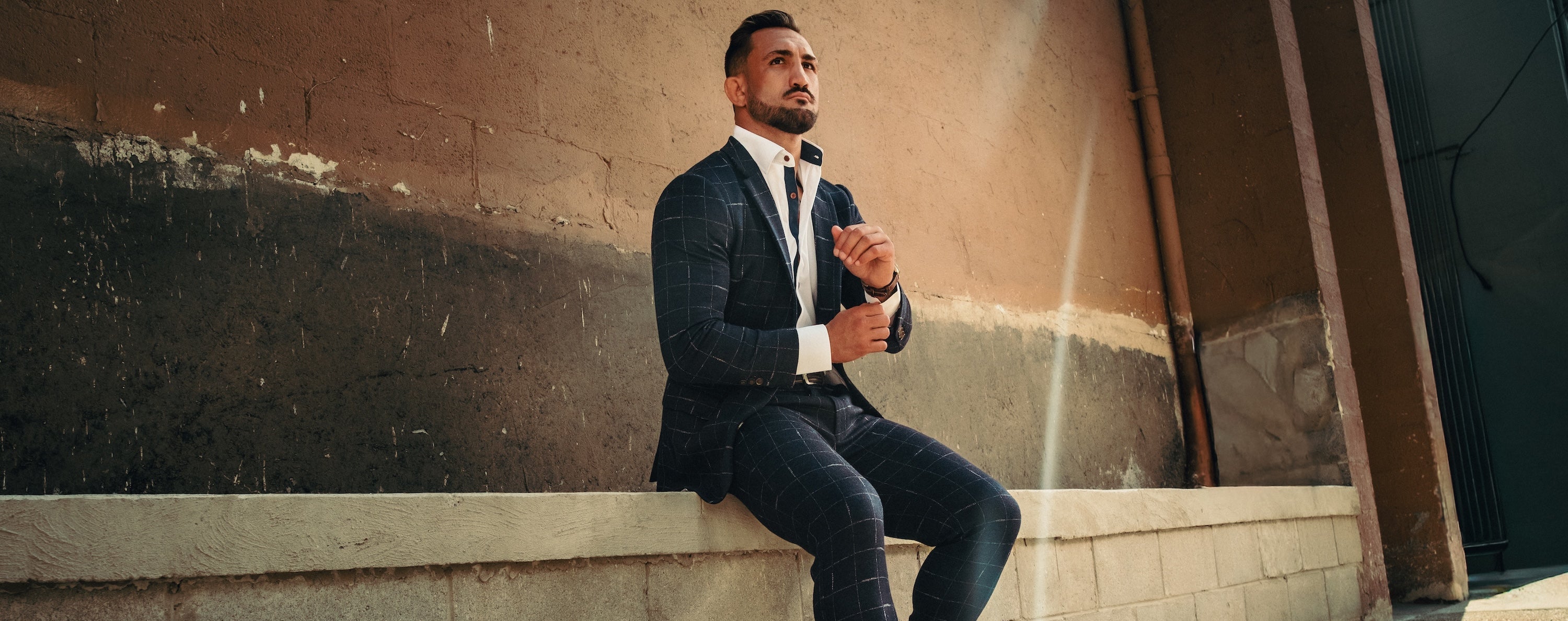 Man in a suit sitting on a ledge against a textured wall