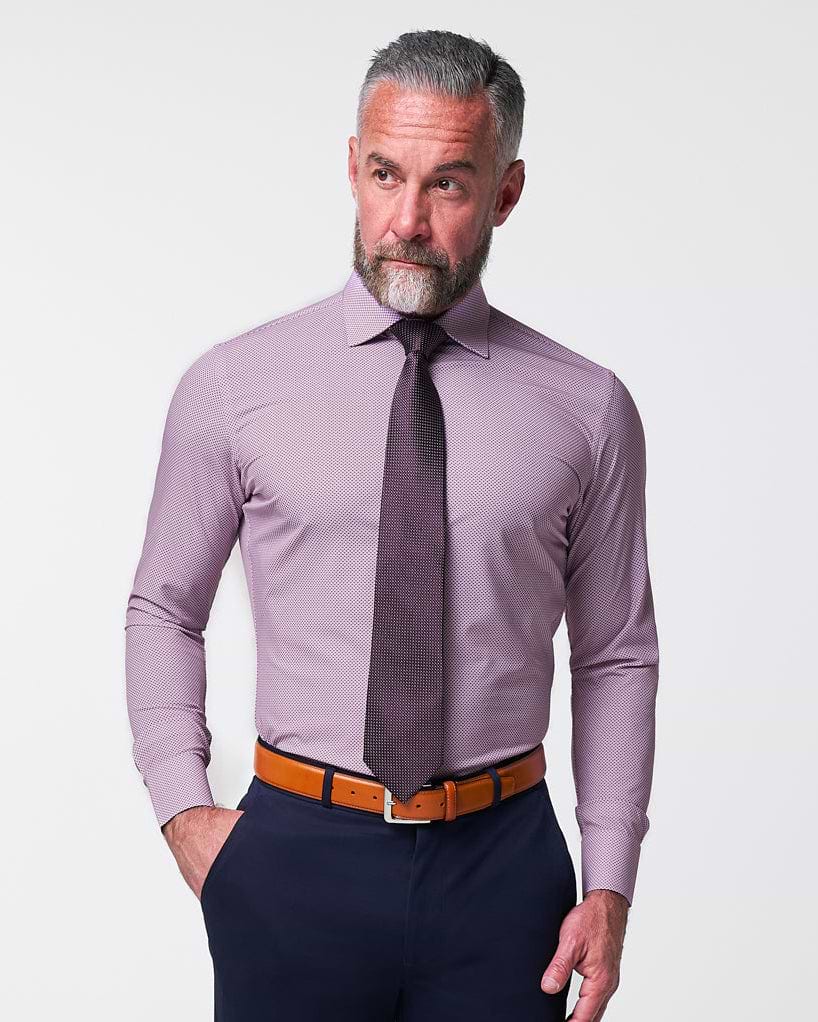 Man wearing a light purple dress shirt, dark tie, and navy pants against a plain background