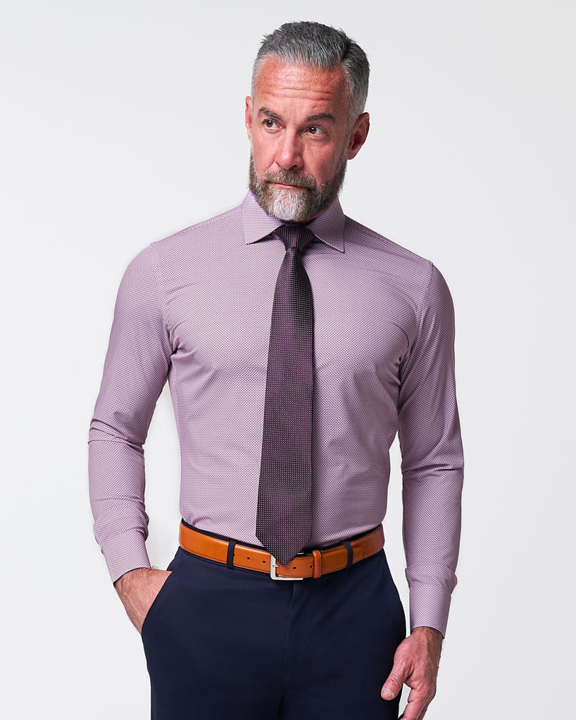 Man wearing a light purple dress shirt, dark tie, and navy pants against a plain background