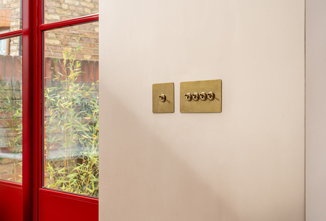 Neutral wall featuring a flush pair of antique brass 'Two Way Toggle Switches', adjacent to a red backdoor.