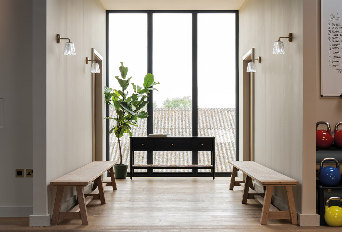 Minimal and tidy walkway kitted out with benches, plants and home furnishings. 'Richmond Fluted Glass Wall Lights' lining the walls.