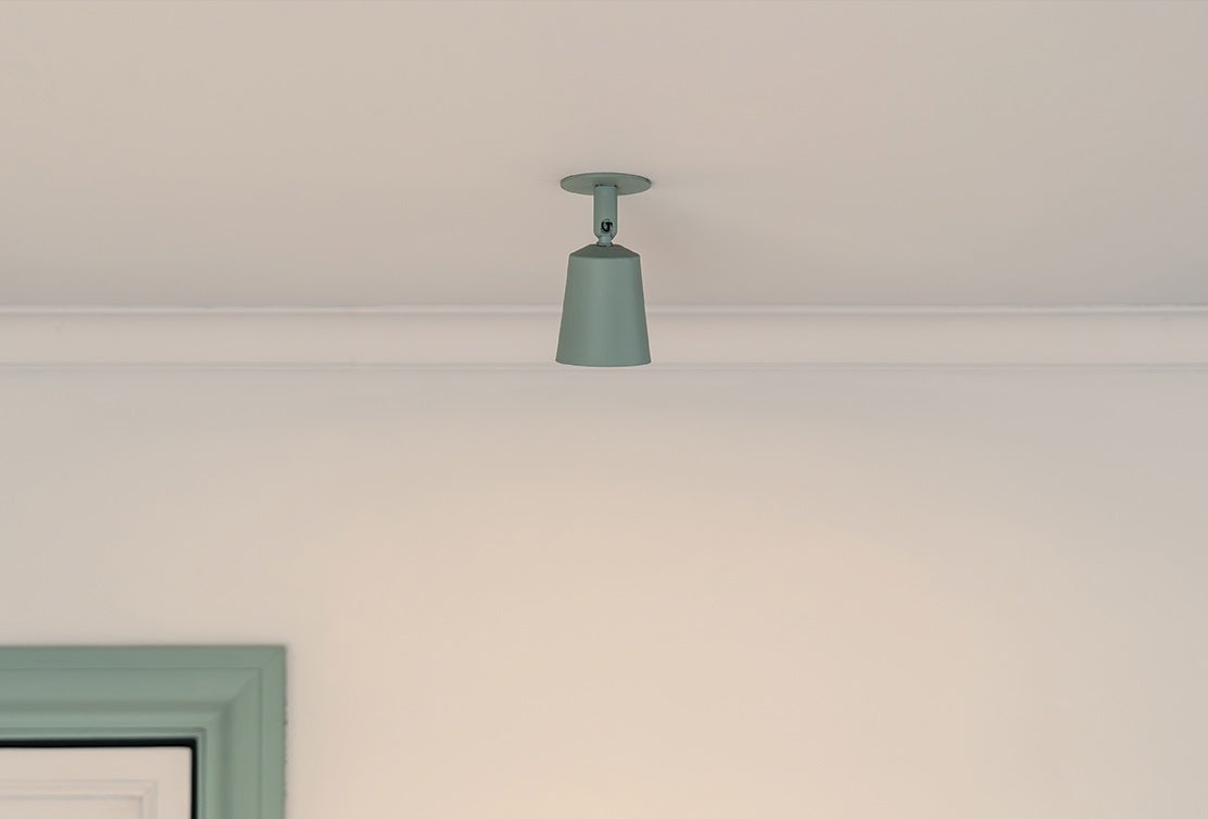 A modern green pendant light hangs from a white ceiling, illuminating the minimalist room below.