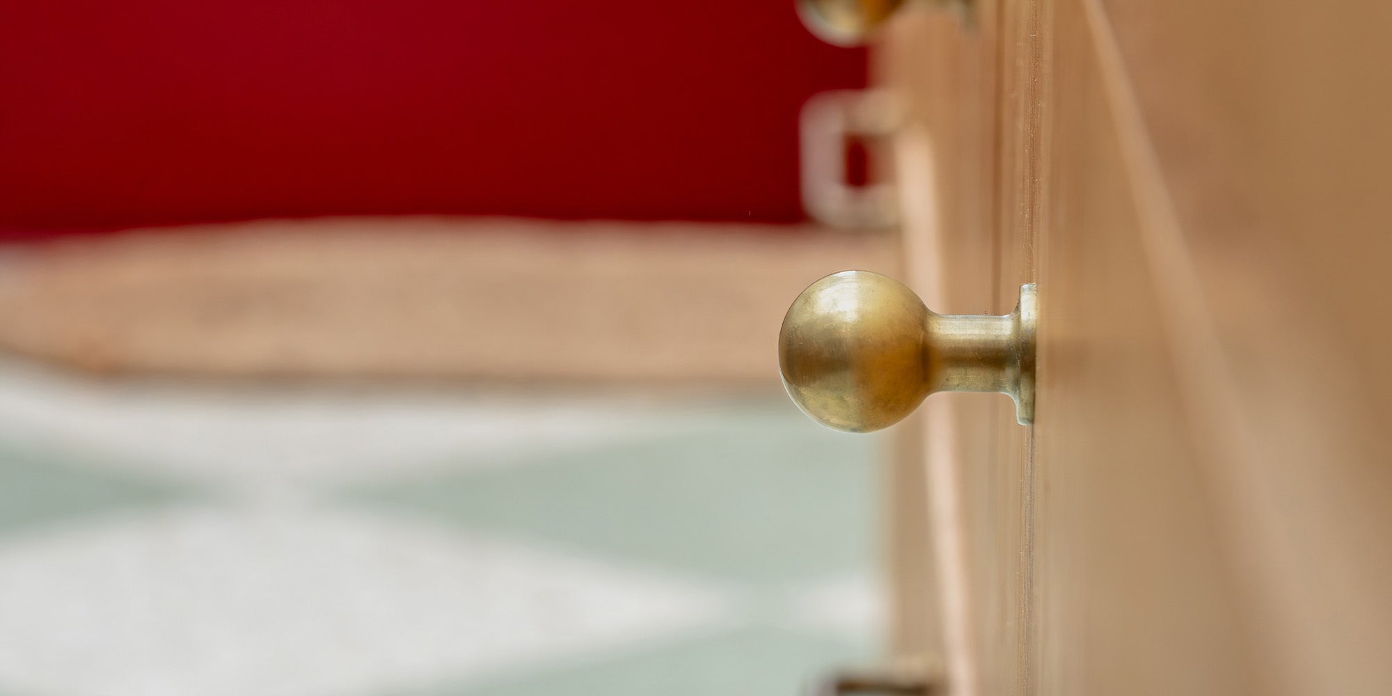 Close-up of a wooden cabinet featuring a simple 'Bayswater Furniture Knob' in an antique brass finish.