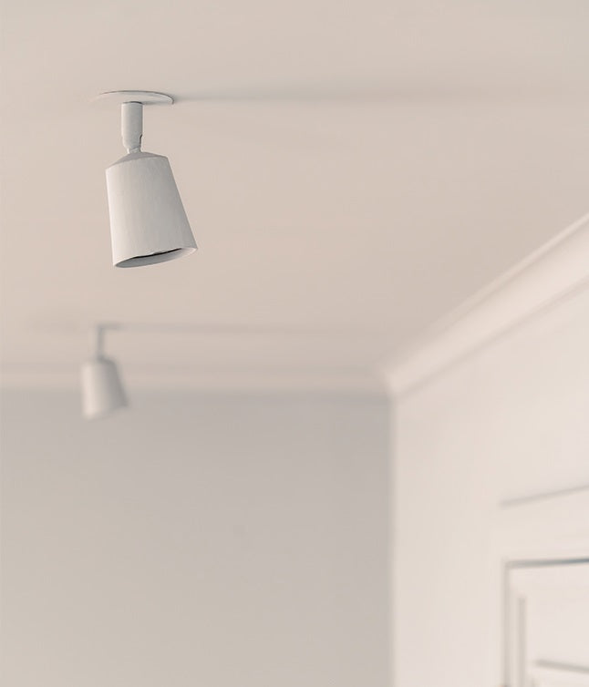 Two minimalist white pendant lights hang from a ceiling in a softly illuminated room with neutral tones.