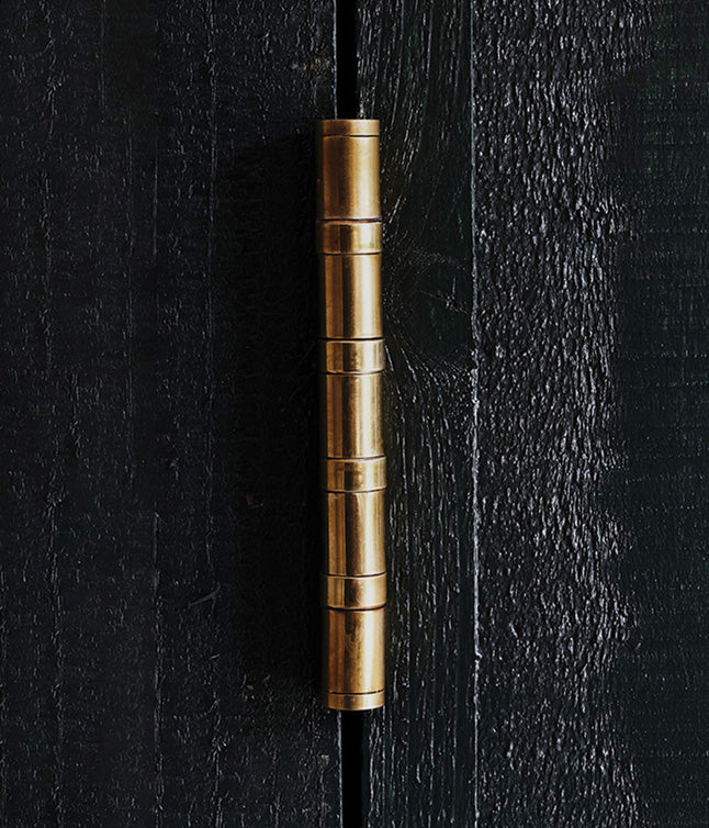Close-up of a dark wooden cabinet with brass handles and hinges against a white wall, showcasing modern design elements.