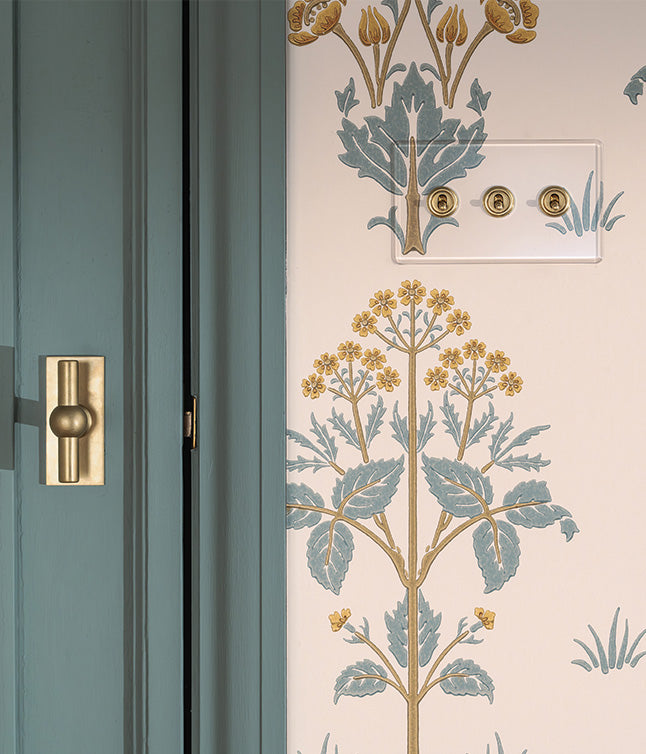 A close-up of a light switch on a floral-patterned wall, featuring elegant blue and gold accents, alongside a teal door trim.