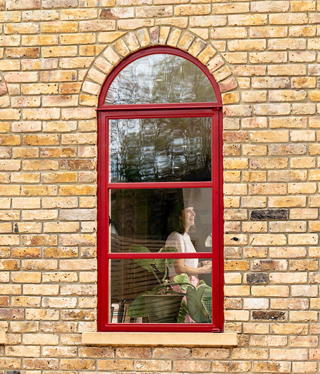A person visibly smiling through a red window frame.