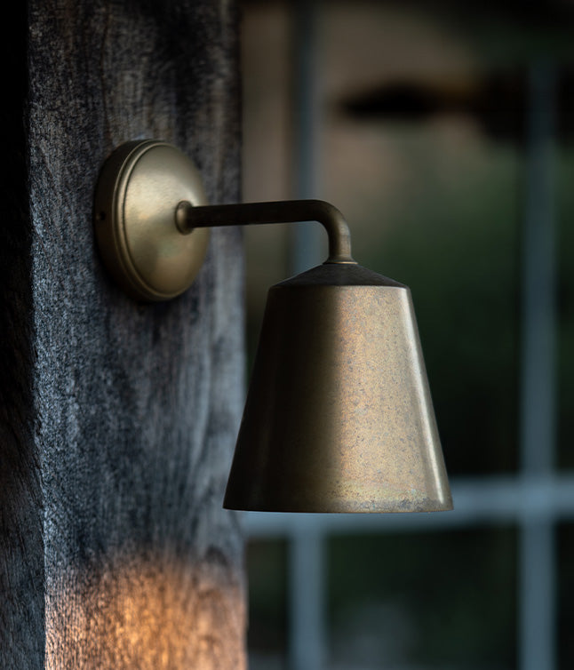 Rustic 'Richmond' wall light in a living antique brass finish, installed on an outdoor wooden surface.
