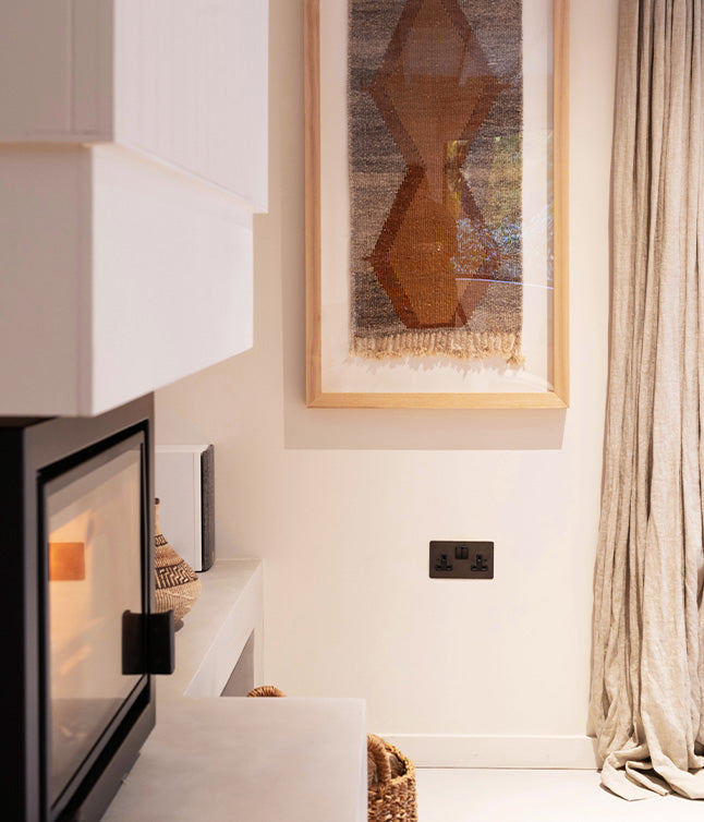 A stylish display of woven wall decor, vases, a pitcher, and a lamp next to a vibrant green plant, set against a neutral wall.