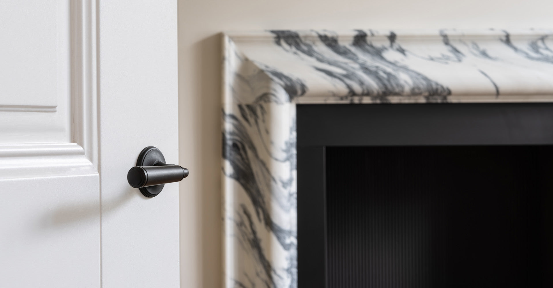 Close-up of a matte black door handle on a white door, beside a marble fireplace mantel with swirling grey patterns.