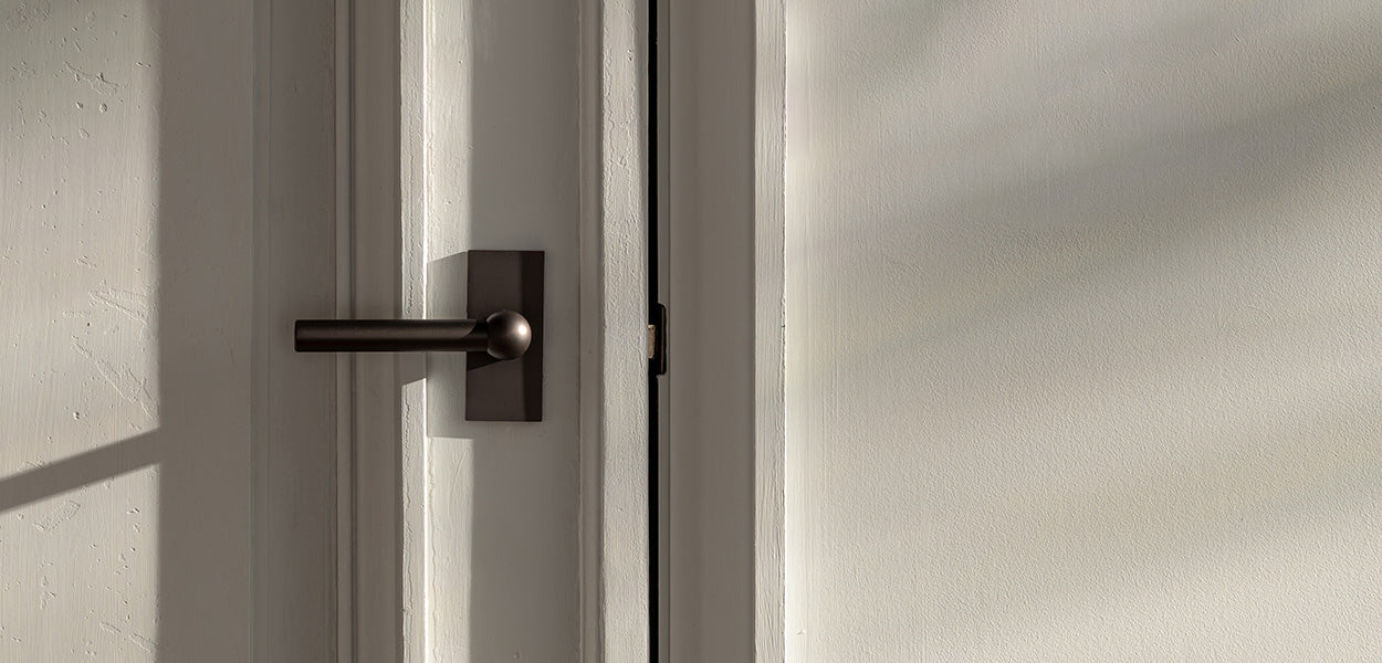 Close-up of a modern door handle on a white door, with soft shadows and light creating a warm, inviting atmosphere.