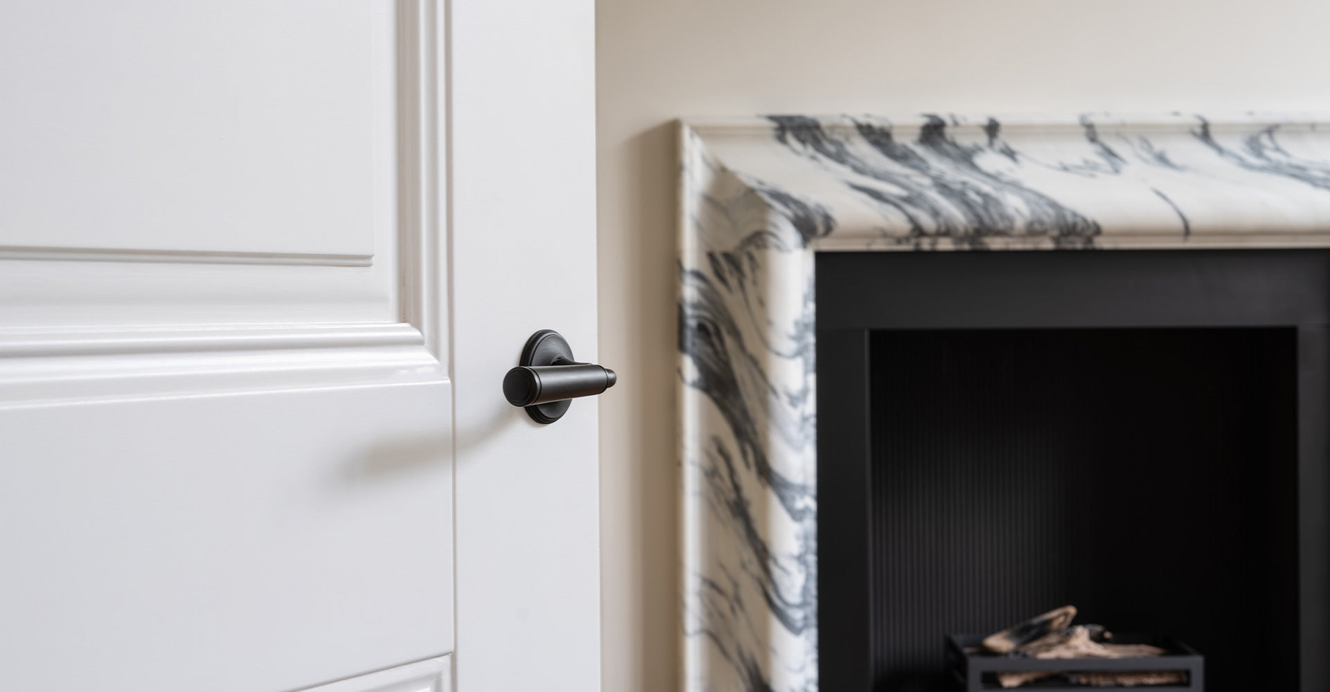Close-up of a sleek black door handle on a white door, with a stylish marble fireplace surround visible in the background.