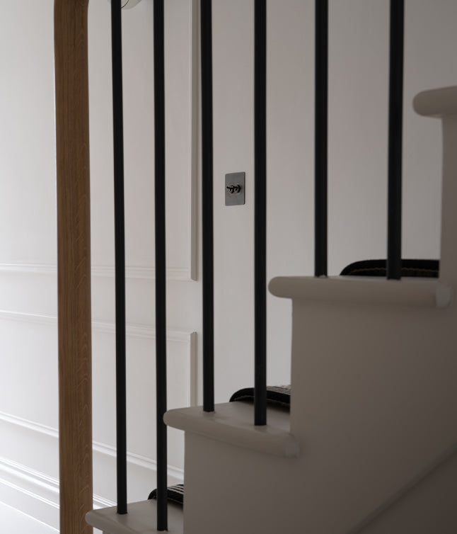 A view of white stairs framed by black railings, leading to a paneled wall, with an elegant wooden door visible in the background.