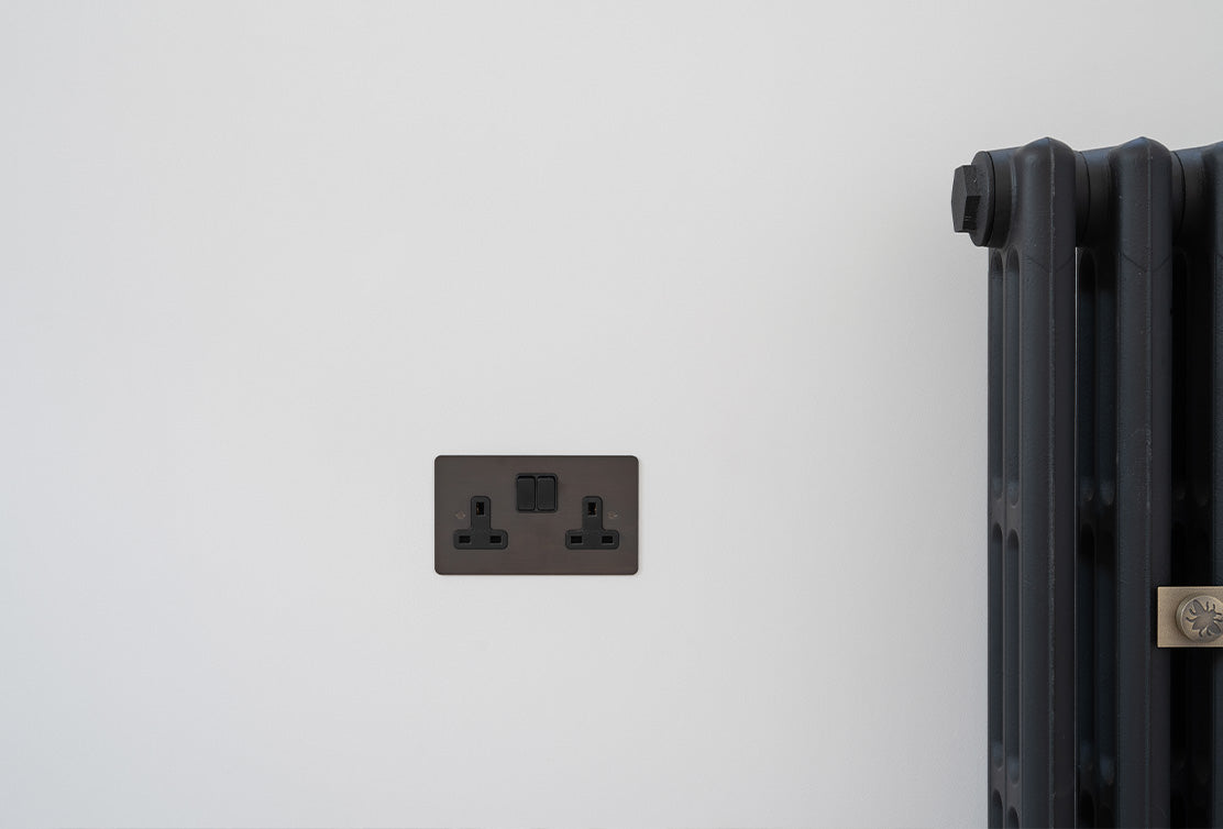 A sleek black electrical outlet on a white wall, adjacent to a dark radiator, showcasing modern interior design elements.