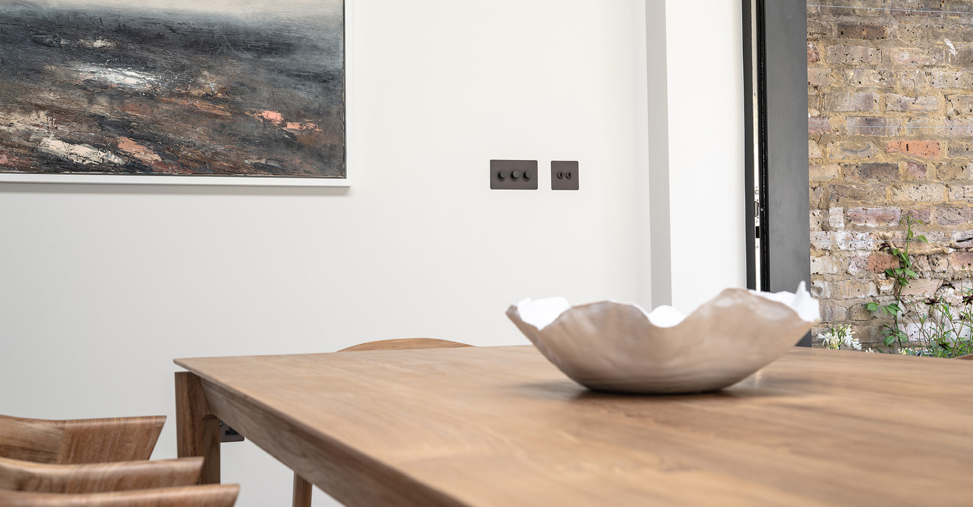 A cozy dining area featuring a wooden table, a decorative bowl, a modern artwork on the wall, and black light switches.