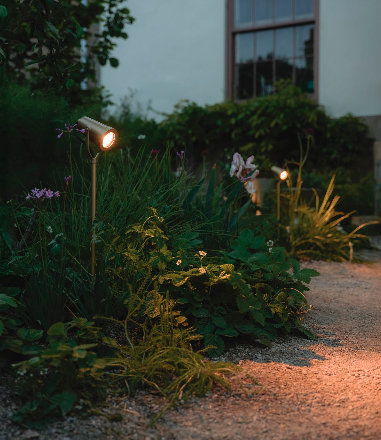 Close-up of two matt bronze 'Ealing Ground Spotlights' in front of a warm blurry backdrop.
