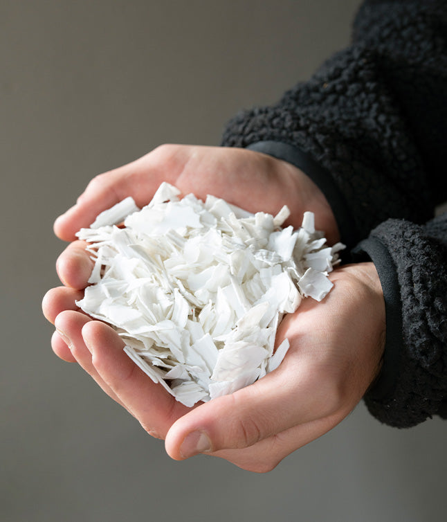 Two hands holding a mound of white, flaked material against a neutral background, suggesting a focus on texture and color.