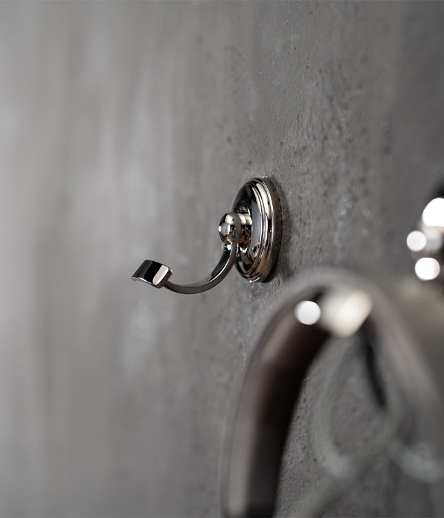 Close-up of a sleek, chrome wall hook mounted on a textured gray wall, showcasing modern design and functionality.