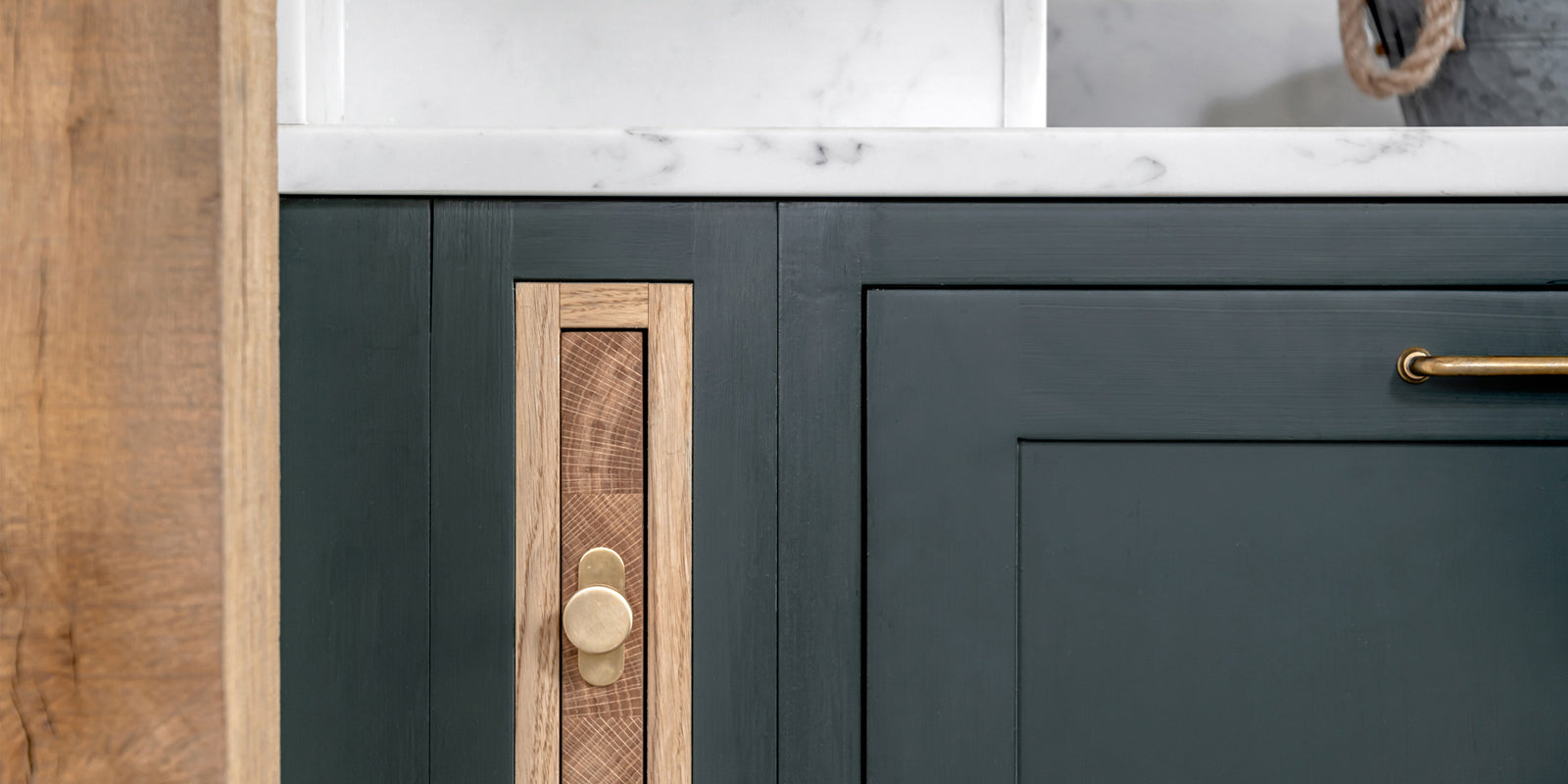Close-up of modern cabinetry featuring dark green paint, natural wood accents, and a circular brass knob for a sleek, contemporary look.