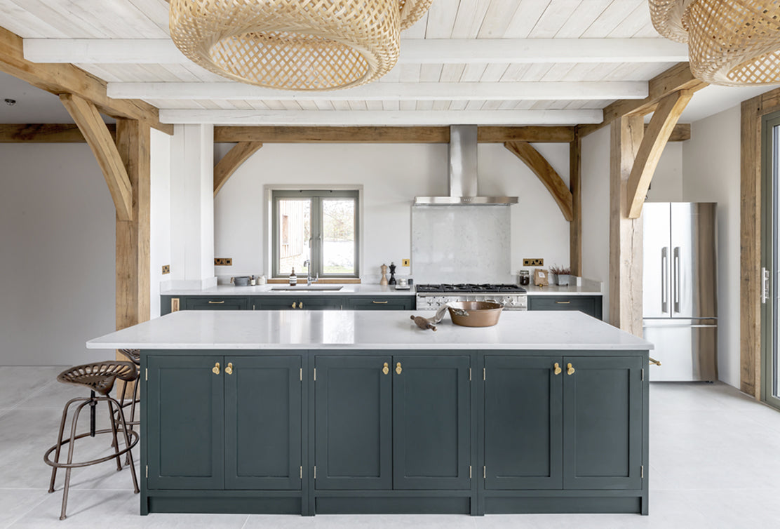 Modern kitchen with dark green cabinetry, white marble countertop, wooden beams, and stylish pendant lights.