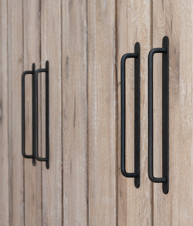 Close-up of black metal handles on wooden cabinet doors with a light, natural wood grain finish.